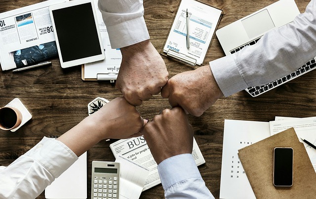 Four people doing a fist bump over a desk, symbolizing partnership and collaboration